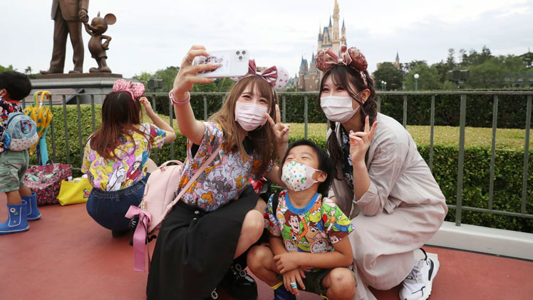 Visitors pose for photo during the reopening of Tokyo Disneyland on July 1, 2020. Disneyland reopened on the same day for the first time in about four months due to an outspread of coronavirus COVID-19. ( The Yomiuri Shimbun via AP Images )