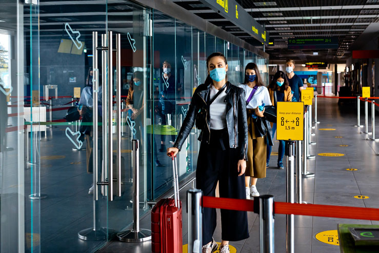 Passengers wearing N95 face masks waiting in line at an airport terminal © izusek / Getty Images