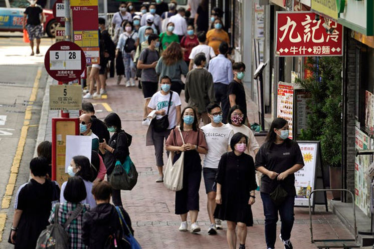 People wearing masks to protect against the coronavirus, walk down a street in Hong Kong. Singapore and Hong Kong have postponed a planned air travel bubble meant to boost tourism for both cities, amid a spike in coronavirus infections in Hong Kong. The air travel bubble, originally slated to begin Sunday, will be delayed by at least two weeks, Hong Kong&rsquo;s minister of commerce and economic development, Edward Yau, said at a news conference on Saturday, Nov. 21, 2020.