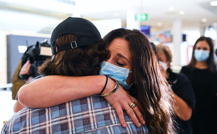 A woman wears a facemask as she hugs her loved one after arriving at the international arrivals area at Sydney's Kingsford Smith Airport ©James D. Morgan/Getty Images