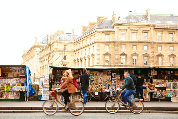 Cyclists passing Bouquinistes (booksellers) on the banks of the Seine. ©Matt Munro/Lonely Planet